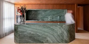 Área gourmet interna do edifício Joya Jardins: design de interiores contemporâneo com bancada em ilha, marcenaria planejada de alto padrão e mobiliário de design para áreas comuns de empreendimentos residenciais.